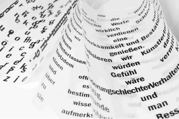Close-up of a swirling sheet of translucent paper printed with German words in black ink.